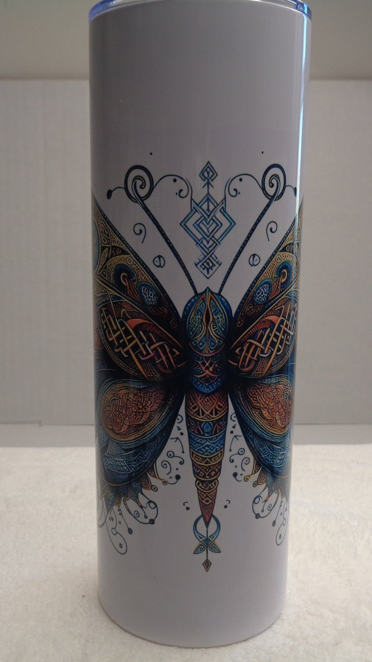 20 oz. insulated tumbler with a lid, featuring a detailed, colorful mandala-style butterfly design on the front, set against a plain indoor background.
