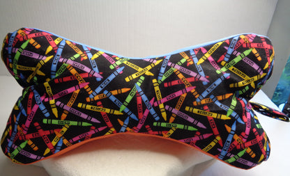 A bone-shaped neck pillow with a black background and a colorful crayon print. 