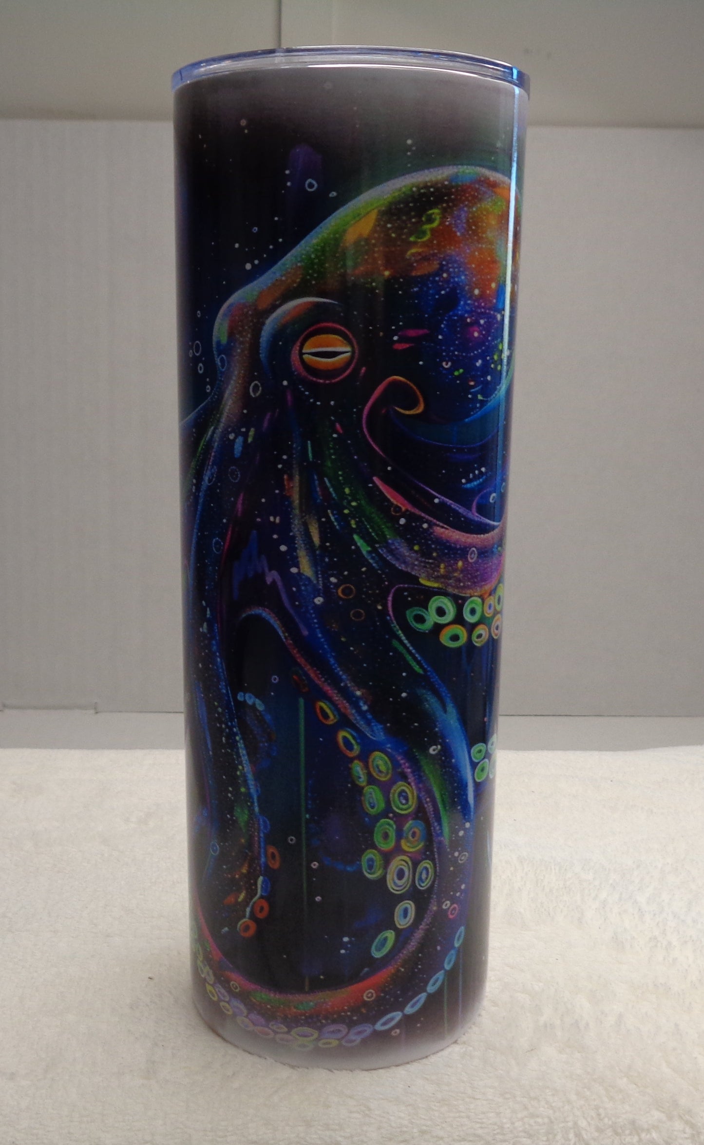 A tall cylindrical tumbler with a colorful octopus design, standing upright on a white towel against a plain indoor background.