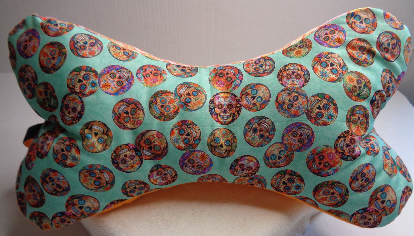 A bone-shaped neck pillow featuring a colorful sugar skull pattern. 