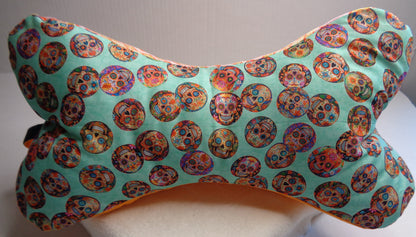 A bone-shaped neck pillow featuring a colorful sugar skull pattern. 