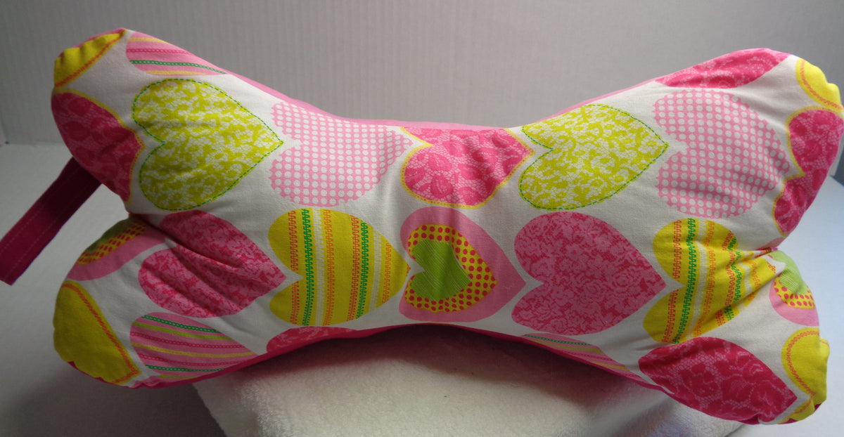 A bone-shaped neck pillow with a colorful heart pattern in pink, yellow, and green. 